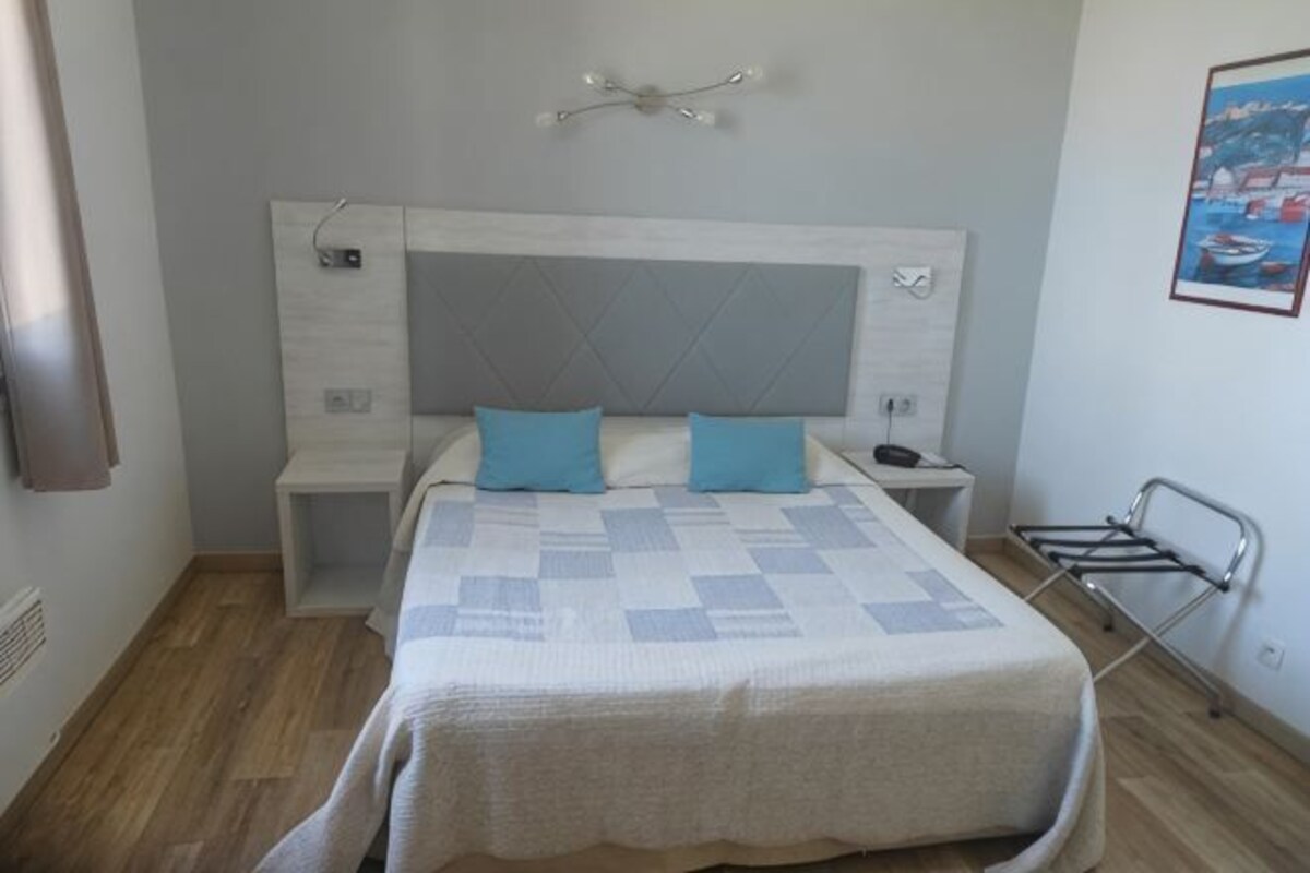 Un dormitorio con cama, mesitas de noche, cabecera y lámpara fijada a la pared.