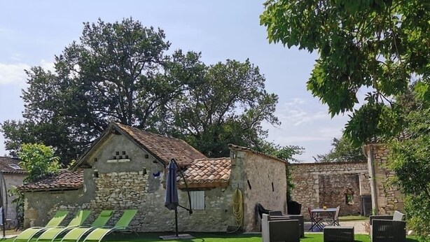 Un espace piscine agrémenté d’un bâtiment en pierre, d’une pelouse verdoyante et de mobilier d’extérieur.