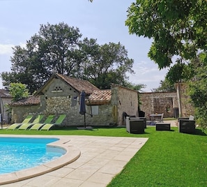A pool area with a stone building, green lawn, and outdoor furniture.