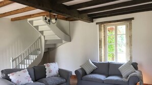 Un salon avec deux canapés gris, un escalier et une fenêtre donnant sur un paysage verdoyant.