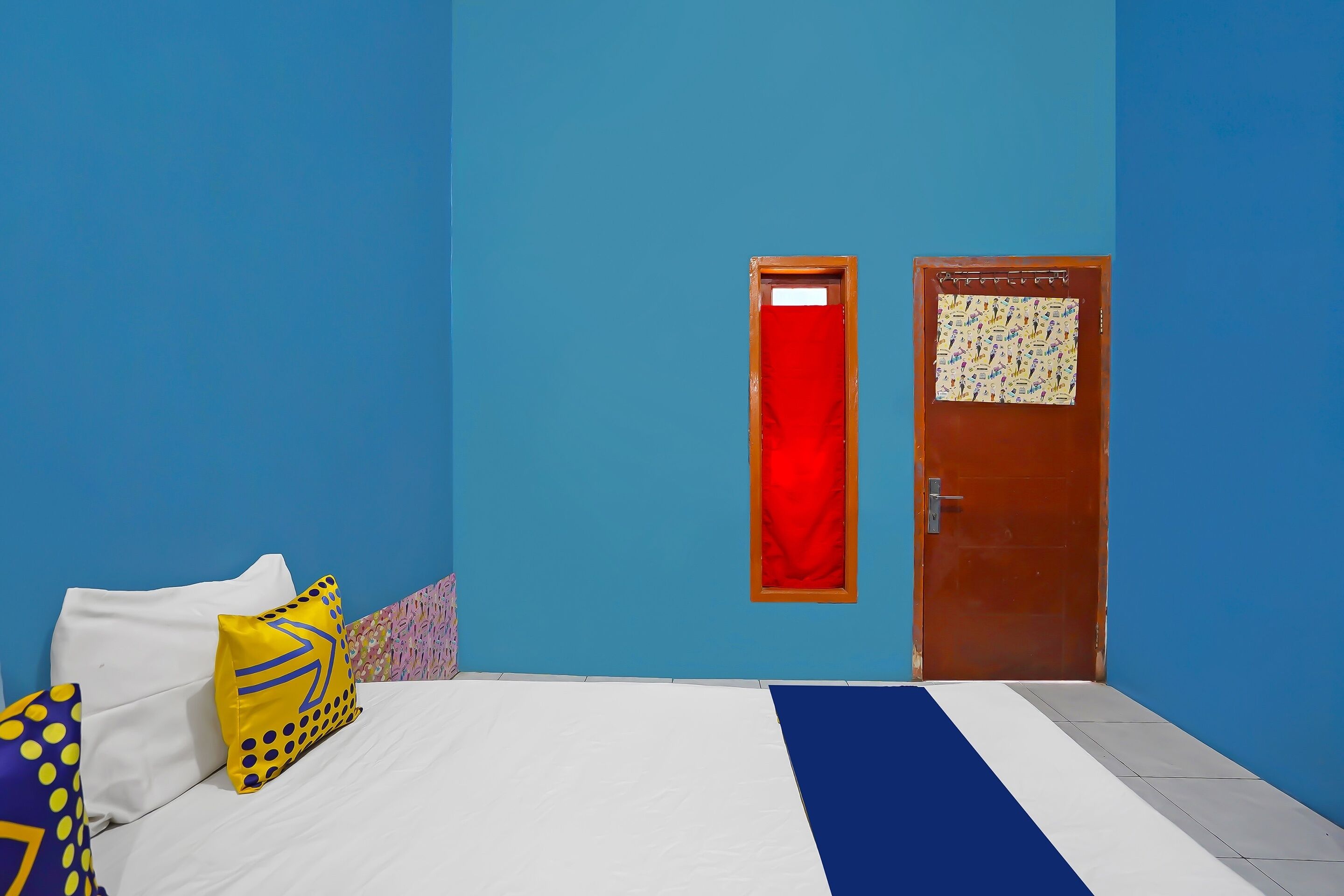 Une pièce avec un lit, une porte et un mur sur lequel est accroché un rideau rouge.