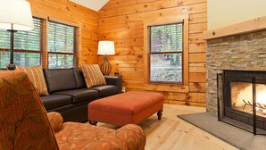 Un interior acogedor de cabaña de madera con chimenea, un sofá y un sillón estampado.