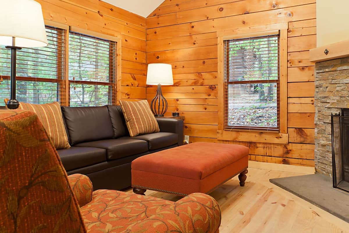 A cozy log cabin interior with a fireplace, a sofa, and a patterned armchair.