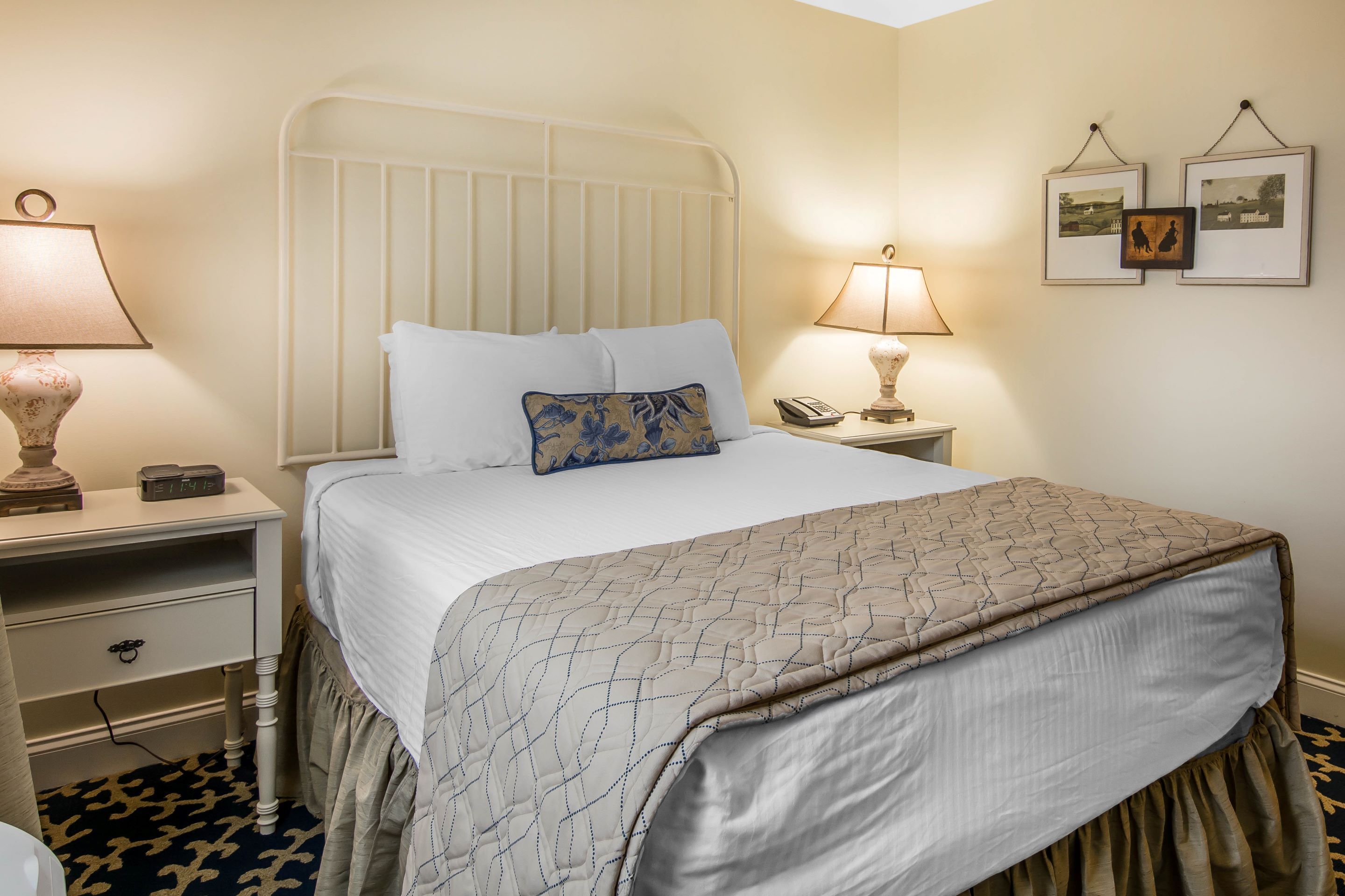 A neatly made bed with a patterned bedspread, a bedside lamp, and a nightstand with a telephone and a decorative item.