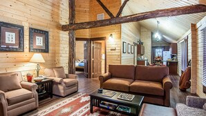 Interior acogedor de una cabaña de madera con sala de estar que incluye un sofá marrón, dos sillones, una mesa de centro y una chimenea.