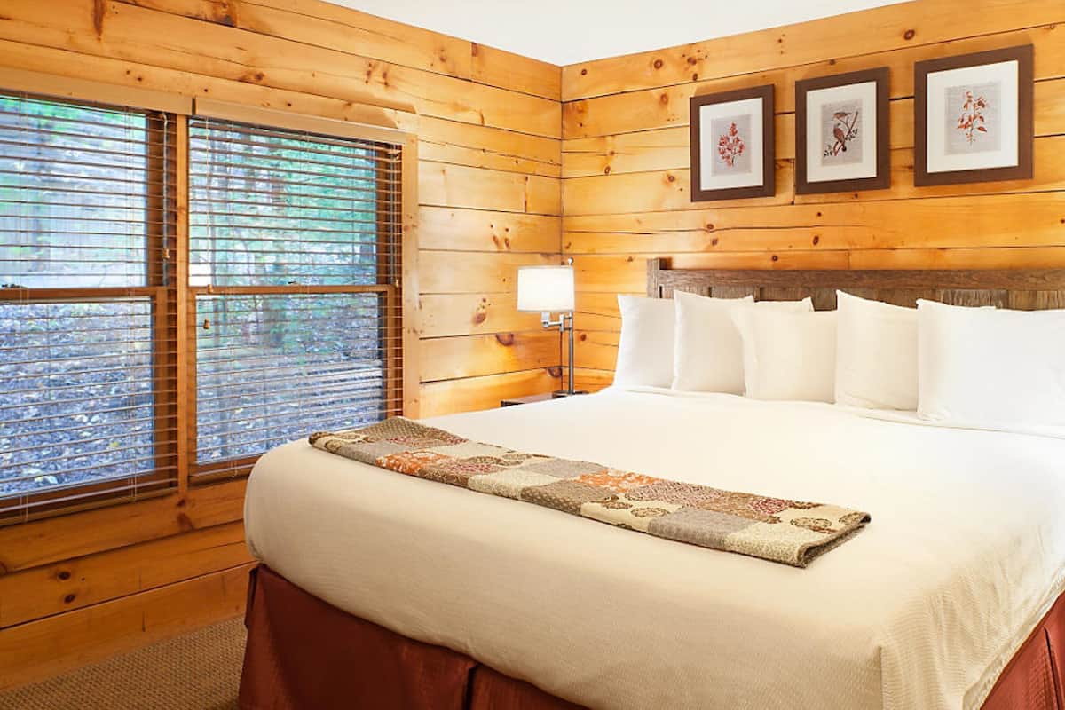 A wooden-paneled bedroom with a large bed, two bedside lamps, and a window with blinds.
