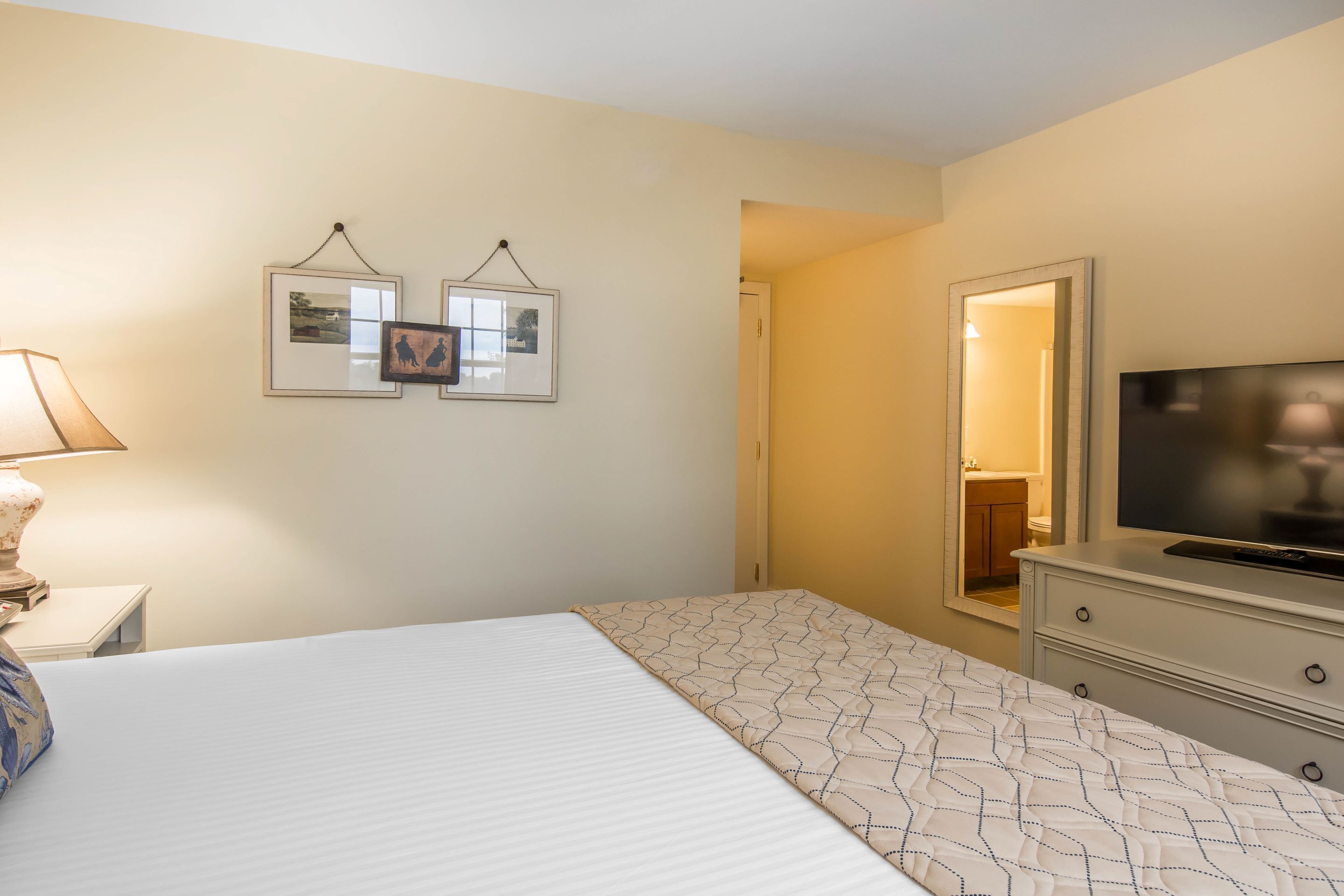 A hotel room with a bed, a TV, a dresser, and two framed pictures on the wall.
