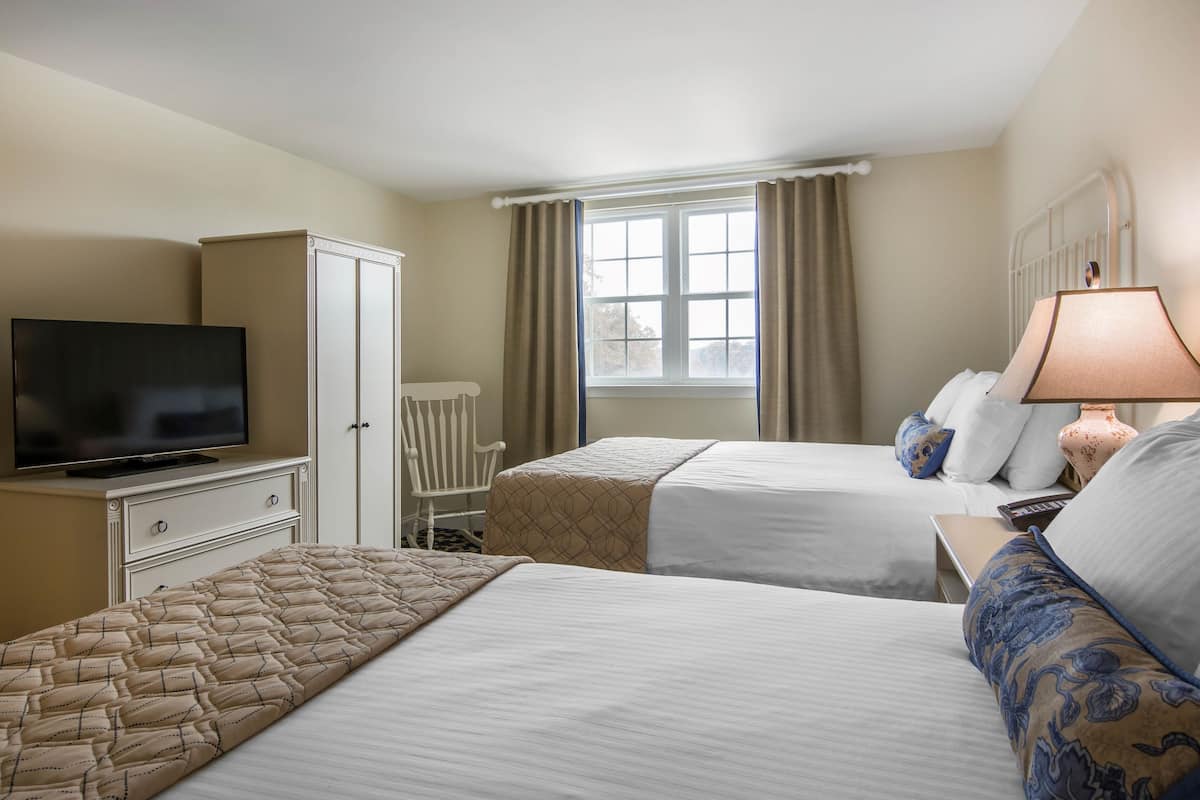 A hotel room with two beds, a television, a desk, and a window with curtains.