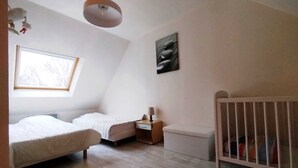 A bedroom with a sloped ceiling, a window, a crib, a bed, and a bedside table with a lamp. - Maison 6 Pers 2 Chambres Bord de mer à Banastère (Sarzeau)