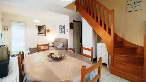 A dining area with a round table, chairs, a staircase, and a sofa. - Maison 6 Pers 2 Chambres Bord de mer à Banastère (Sarzeau)