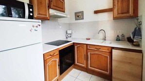 A compact kitchen with wooden cabinets, a built-in oven, a microwave, and a sink. - Maison 6 Pers 2 Chambres Bord de mer à Banastère (Sarzeau)