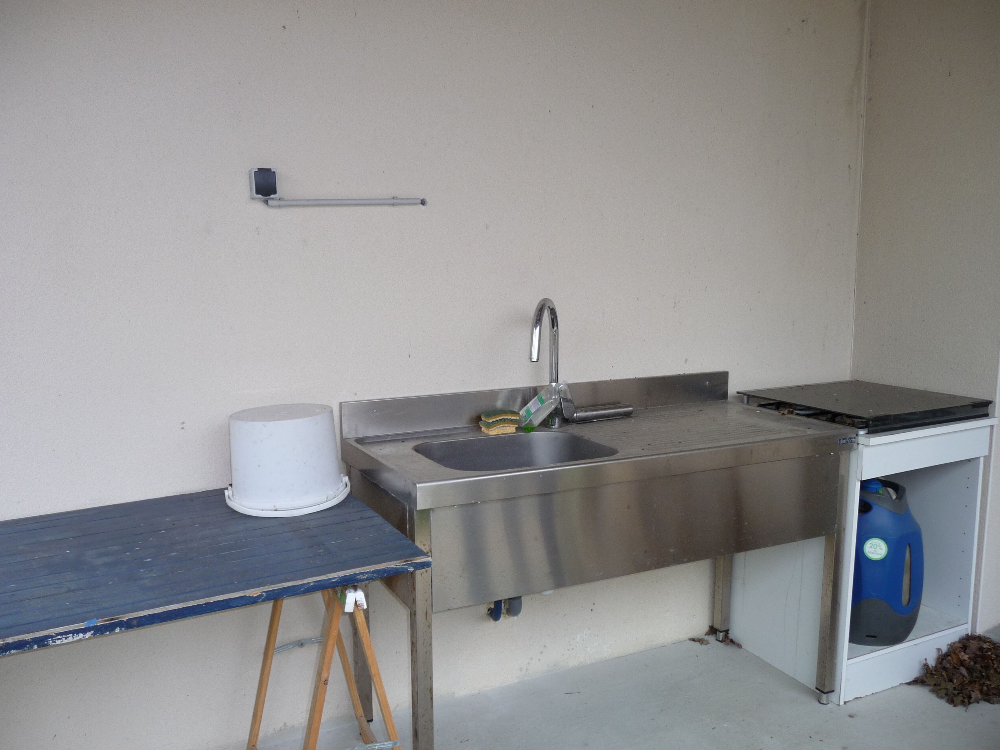 A small kitchenette with a sink, a stove, and a trash bin.