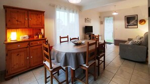 A dining area with a round table, wooden chairs, and a cabinet with a light on top. - Maison 6 Pers 2 Chambres Bord de mer à Banastère (Sarzeau)