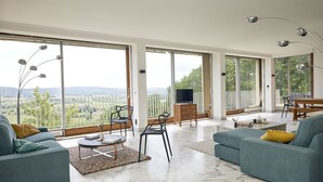 Un salón amplio con ventanas grandes, una televisión de pantalla plana y un balcón con vistas al campo.