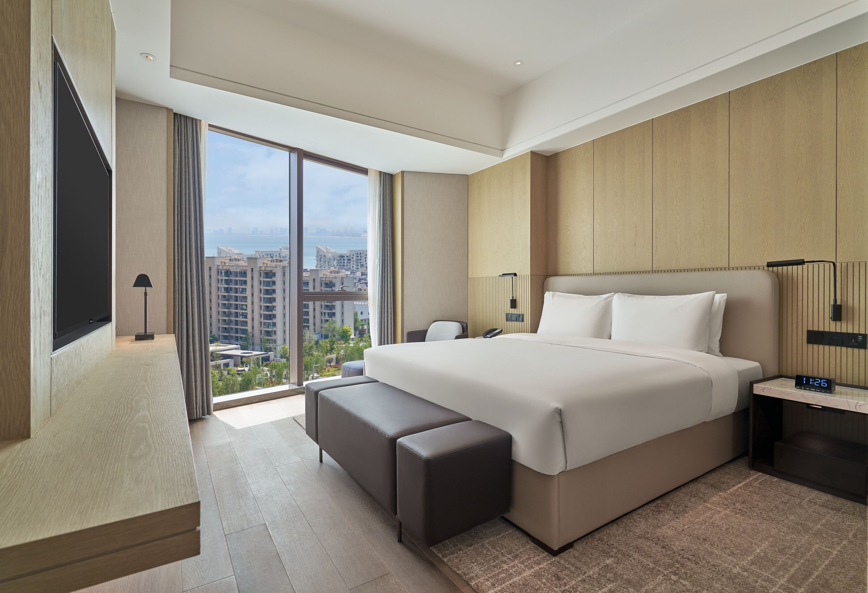 Un moderno cuarto de hotel con una cama grande, un escritorio, una silla, un televisor y vistas a la ciudad.