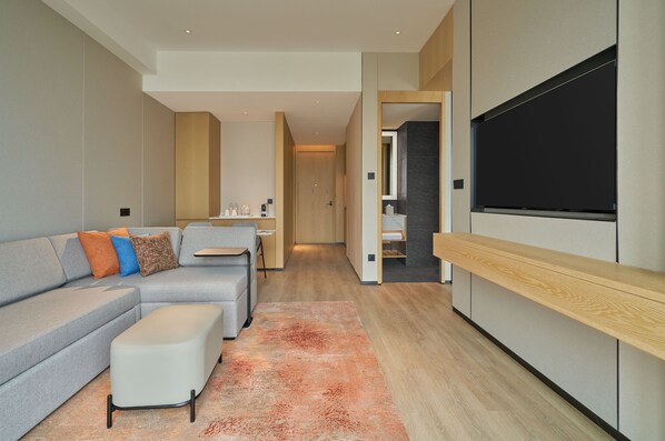 A modern living room with a grey sectional sofa, a white ottoman, and a wooden TV stand. - Hyatt Place Yantai Development Zone (Yantai)