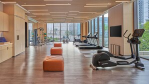 A modern gym with treadmills, elliptical machines, and orange ottomans.