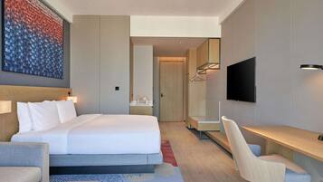 A modern hotel room with a large bed, a desk, a chair, a TV, and a wardrobe.