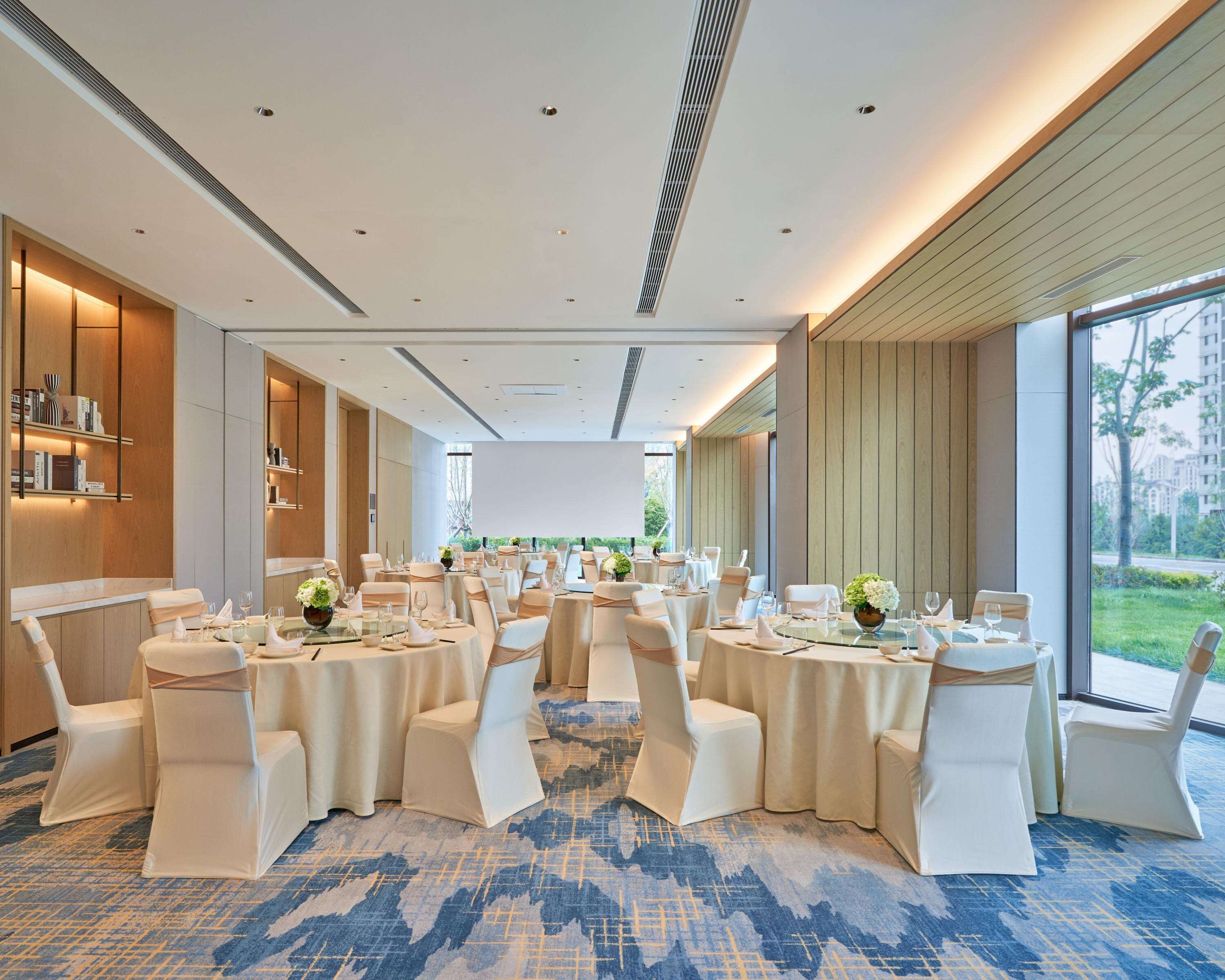 A conference room with round tables, white chairs, and a carpeted floor.