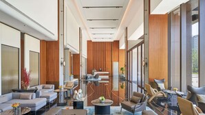 A modern hotel lobby with a central seating area, a reception desk, and large windows offering views of the outdoors.