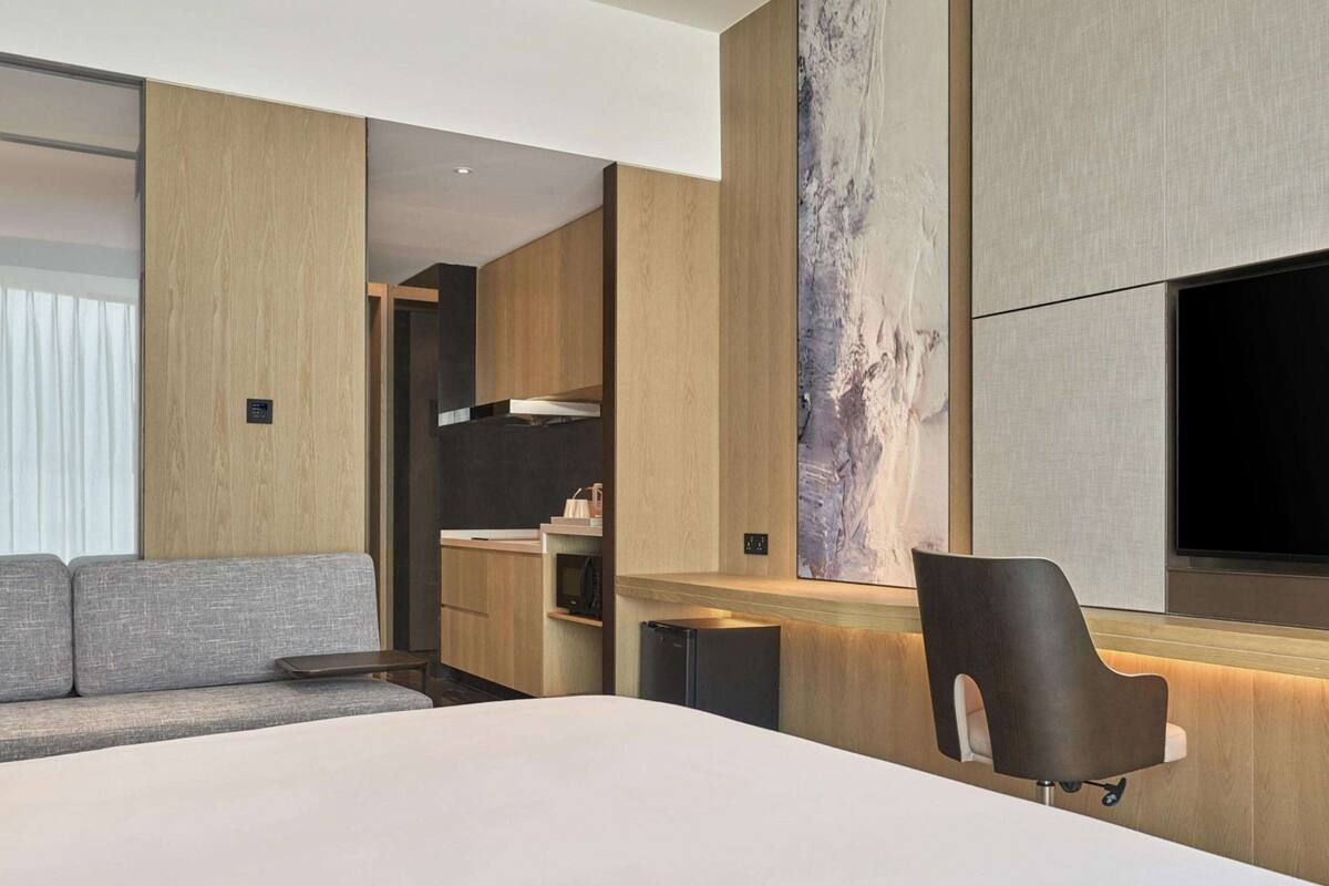 A modern hotel room with a large bed, a desk with a chair, a television, and a large abstract painting on the wall.