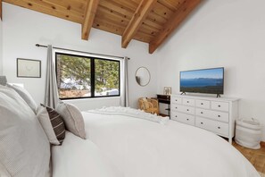 A bedroom with a large bed, a dresser, a television, and a window with a view of trees and mountains.
