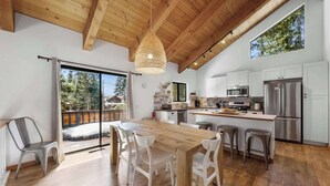 Une cuisine moderne avec des poutres en bois, un grand îlot central, des armoires blanches et une vue sur l’extérieur.