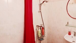 Un baño con ducha, repisa de vidrio con artículos de aseo y lavamanos.