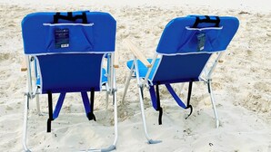 Zwei blaue Liegestühle am sandigen Strand mit freiem Blick auf das Meer.
