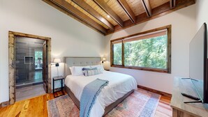 A bedroom with a large bed, two bedside lamps, a window with a view of trees, and a wooden ceiling. - Private Hot tub, 1mi to Shangri La, next to Battlefield Par 3, & Walk to Lake (Afton)