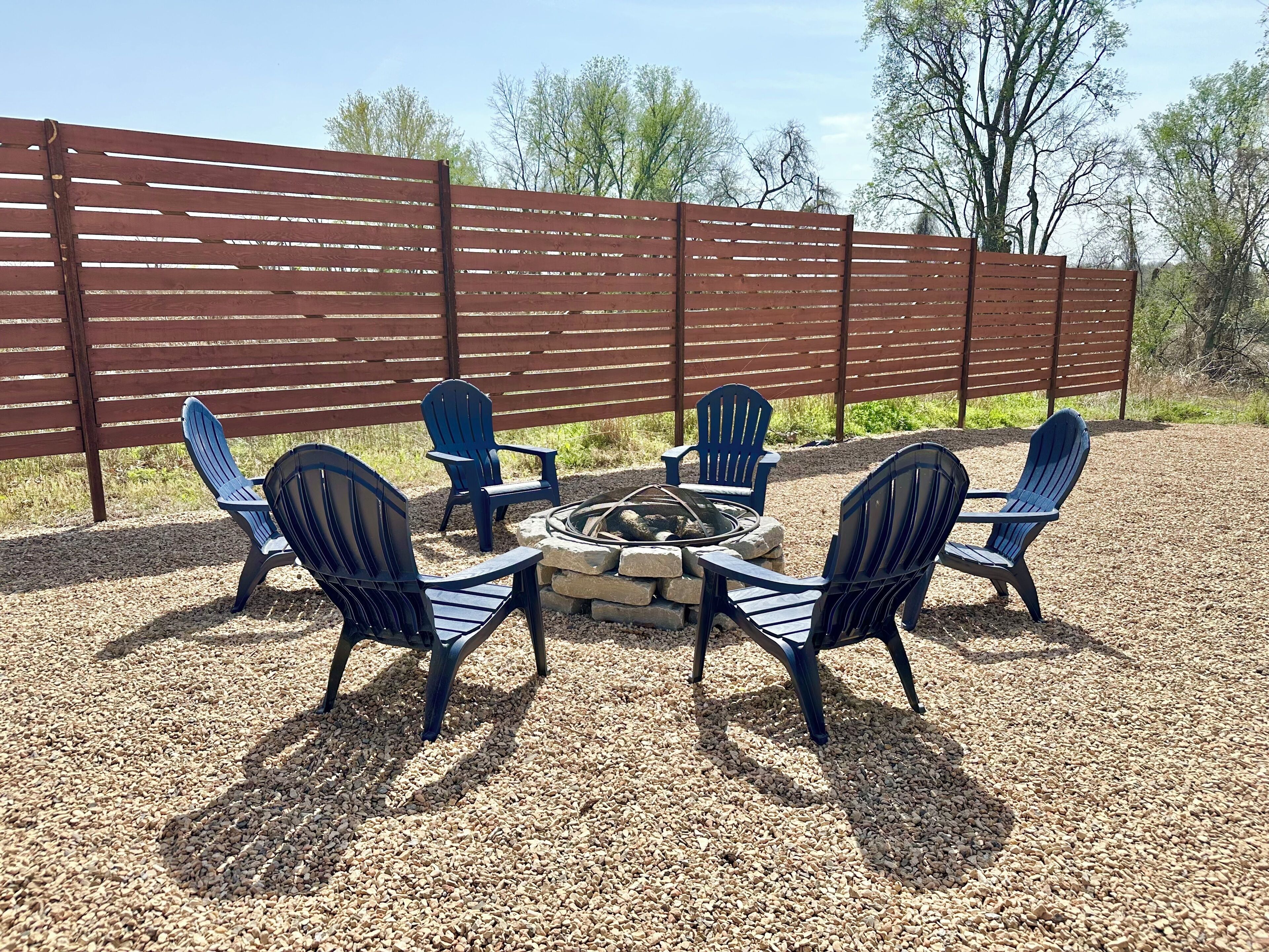 Een patio met een vuurkorf en vier Adirondack-stoelen eromheen.
