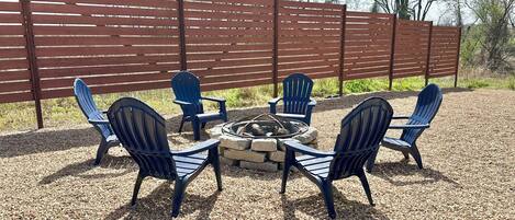 Un patio con una chimenea y cuatro sillas Adirondack dispuestas a su alrededor.