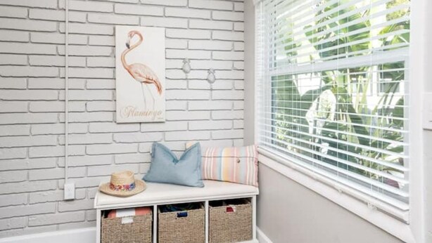 A room with a white brick wall, a framed flamingo artwork, a bench with cushions, and baskets. - Comfortable , newly remodeled, close to Siesta Key (Sarasota)