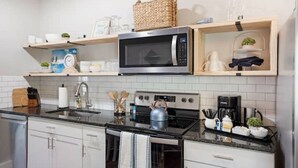 A modern kitchen with a microwave, stove, and sink. There are wooden shelves above the counter holding various kitchen items. - Comfortable , newly remodeled, close to Siesta Key (Sarasota)