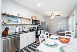 Une cuisine moderne avec des meubles blancs, un lave-vaisselle en acier inoxydable et un coin repas comprenant une table et des chaises blanches.