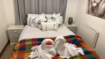 A hotel room with a bed, a colorful checkered blanket, and two white towels shaped like swans.