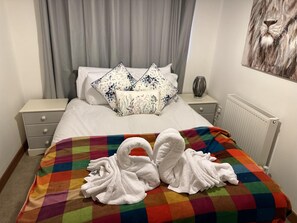 A hotel room with a bed, a colorful checkered blanket, and two white towels shaped like swans. - Luxurious 2-bed Apartment in Maidstone Kent (Maidstone)