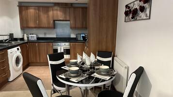 A compact kitchen with wooden cabinets, a built-in washing machine, and a dining area with a round table and four chairs.