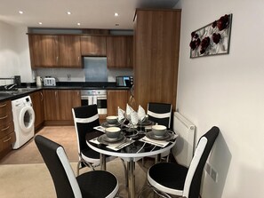 A compact kitchen with wooden cabinets, a built-in washing machine, and a dining area with a round table and four chairs. - Luxurious 2-bed Apartment in Maidstone Kent (Maidstone)