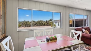 A dining area with a table set for two, a window with a view of trees and a building, and a red couch in the background. - Cosy Desert Hideaway (Tucson)