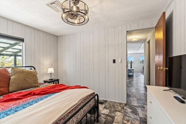A bedroom with a bed, a TV, and a desk. There is a window and a door leading to another room. - Cosy Desert Hideaway (Tucson)