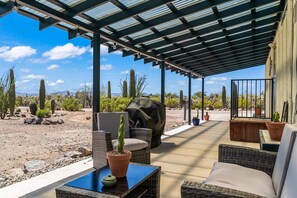 A covered patio with wicker furniture, a cactus planter, and a grill. - Cosy Desert Hideaway (Tucson)