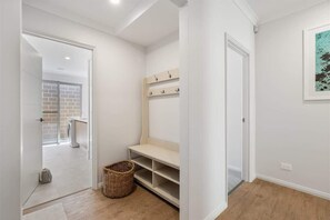 A hallway with a white door, a wicker basket, a bench, and a wall-mounted shelf with hooks.