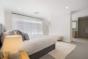 A modern bedroom with a bed, bedside lamp, and a bathroom with a shower and toilet.