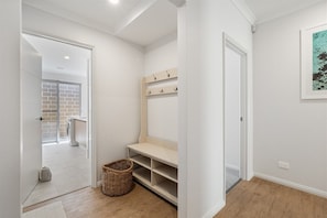 A hallway with a wooden floor, a white door, a wall-mounted shelf with hooks, and a basket on the floor.
