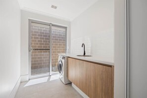 A laundry area with a washing machine, a sink, and a sliding glass door leading to a brick wall.