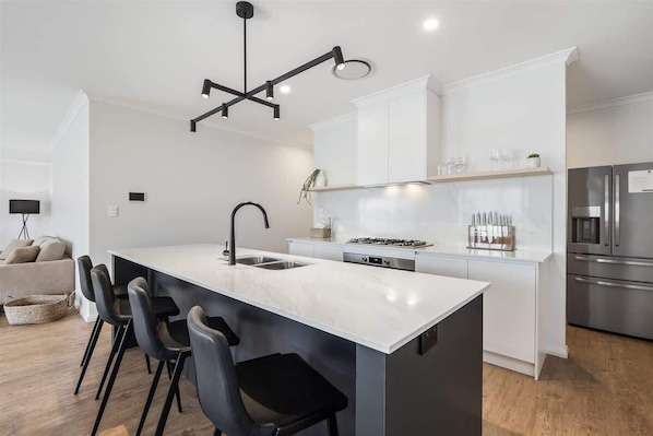 A modern kitchen with a central island, white cabinetry, a stainless steel refrigerator, and a pendant light.