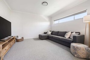 A modern living room with a sectional sofa, a flat-screen TV, a wooden entertainment unit, and a large window.