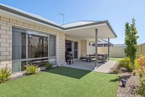 A modern house with a covered patio, a barbecue area, and a well-maintained lawn.