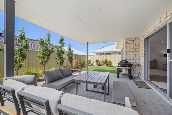 An outdoor patio area with a sofa, a table, and a barbecue grill.